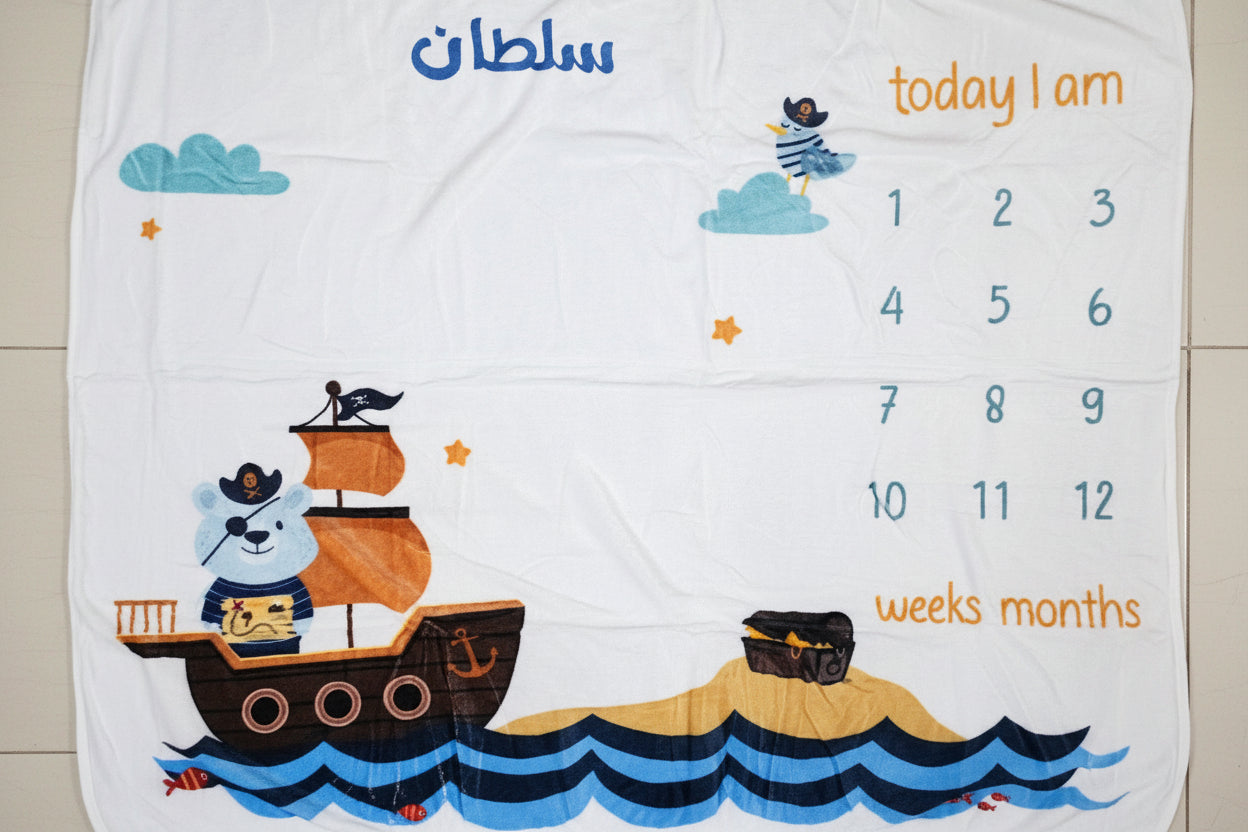 Baby milestone blanket with pirate design and month markers on a tiled floor.