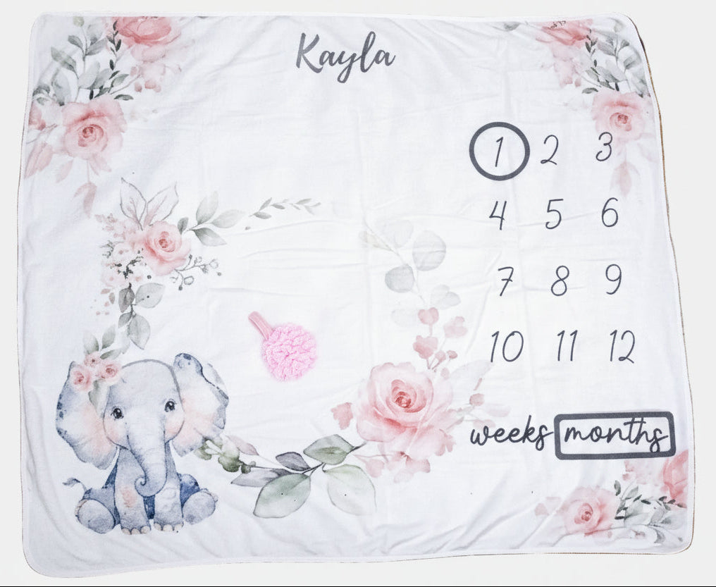 Baby milestone blanket with elephant design and numbers on a floral patterned surface.