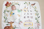 Baby lying on a milestone blanket with animal illustrations and number markers.
